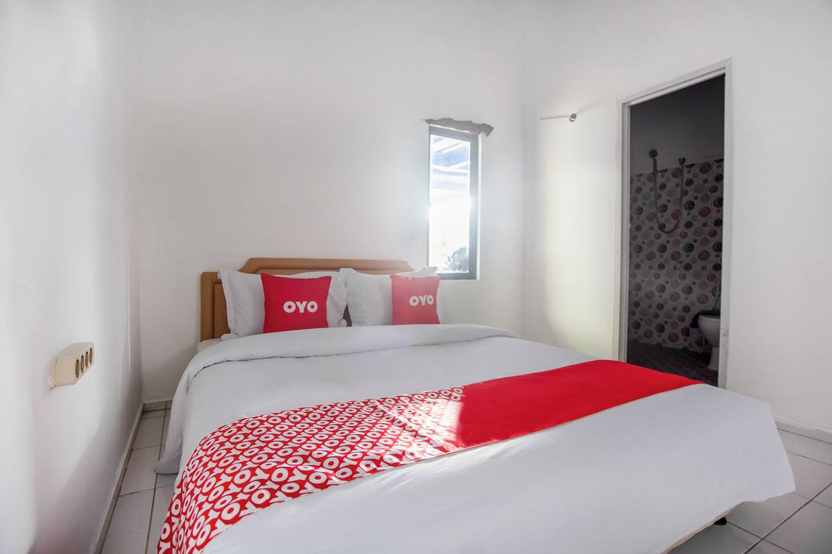 A bedroom with a bed, pillows, a window, and a shower area.