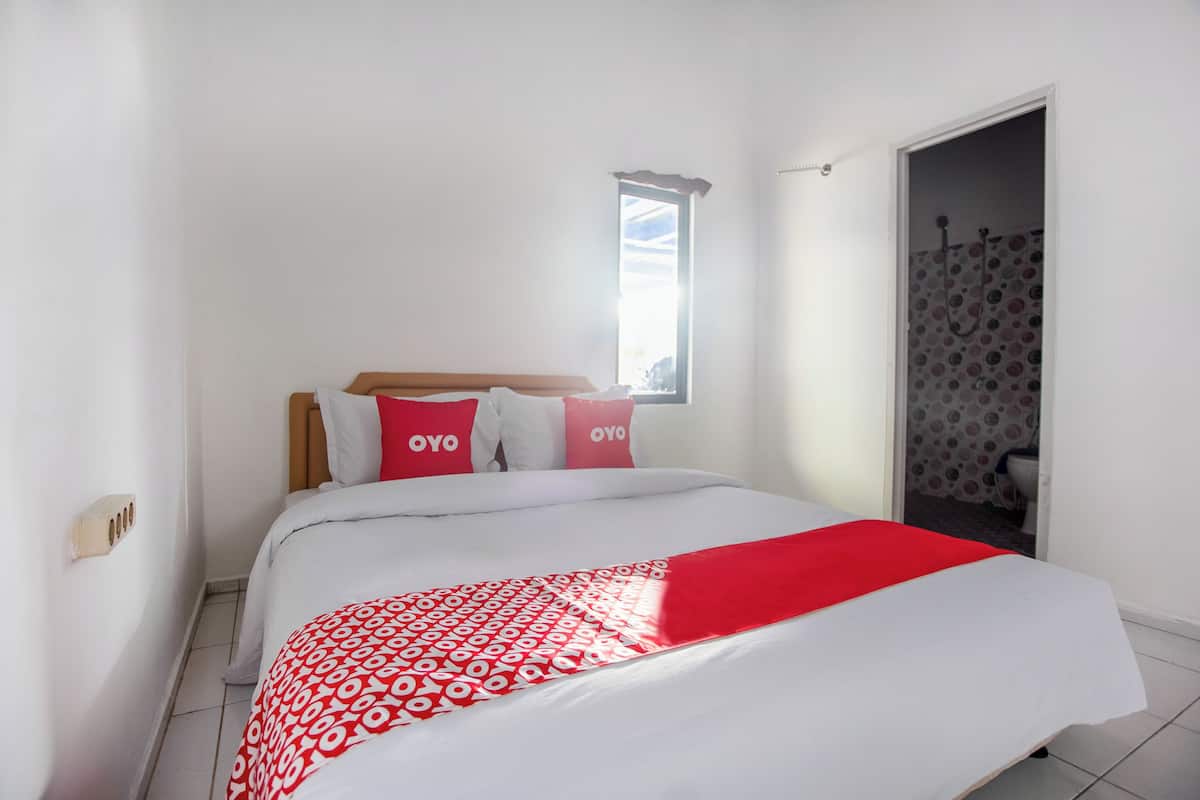 A bedroom with a bed, pillows, a window, and a shower area.