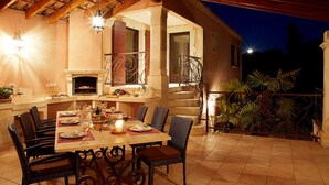 Un área de comedor al aire libre con una mesa lista para comer, rodeada de sillas de mimbre y una chimenea.
