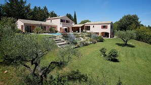Una casa grande de dos pisos con piscina, rodeada por un jardín cuidado y árboles.