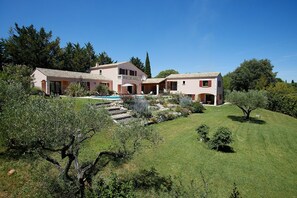 Une grande maison à deux étages avec une piscine, entourée d’un jardin bien entretenu et d’arbres.