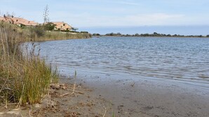 A coastal scene with a sandy beach, a calm body of water, and a building with a tiled roof in the background. - Cozy Studio Mezzanine with A/C, BBQ, Near Beach & Shops - Sleeps 4, Gruissan (Gruissan)