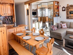 A cozy, well-lit room with a wooden dining table set for four, a sofa with decorative pillows, and a bookshelf filled with books and decorative items. - Ski-In/Ski-Out Apartment in Val Thorens - Sleeps 5, South-Facing Balcony, Renovated (Val Thorens)