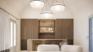 Un salon moderne doté d’un grand canapé en forme de L, d’une table basse ronde et d’un coin cuisine avec des meubles en bois et des luminaires suspendus.