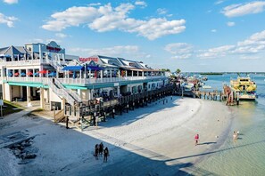 A beachfront hotel with a pier extending into the water, featuring multiple dining areas and a lifeguard station.