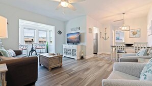 Un salon spacieux doté d’un ventilateur de plafond, d’une télévision et d’un coin repas agrémenté d’un lustre.