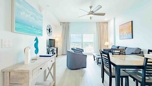 Quarto de hotel moderno com área de refeições, sofá, escrivaninha e uma grande janela com cortinas.