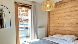Ein Schlafzimmer mit Bett, einem Holzkopfende, einem Fenster mit Blick auf ein Holzgebäude und einer Pendelleuchte.