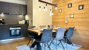 Eine moderne Küche mit dunklen Schränken, einem eingebauten Ofen und einem Essbereich mit einem Holztisch und grauen Stühlen.