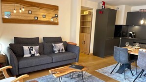 Ein modernes Wohnzimmer mit grauem Sofa, Holztisch und einem Essbereich mit Holztisch und grauen Stühlen.