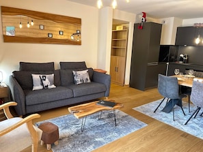 Ein modernes Wohnzimmer mit grauem Sofa, Holztisch und einem Essbereich mit Holztisch und grauen Stühlen.