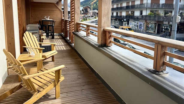 Eine Holzterrasse mit Liegestühlen und einem Tisch, mit Blick auf eine Straße mit Gebäuden und Autos.