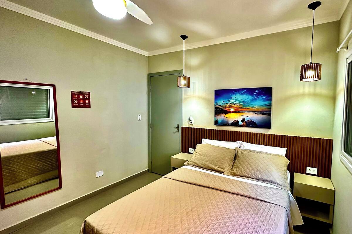 Une chambre d’hôtel avec un lit, une table de chevet, un téléviseur fixé au mur, un tableau et une fenêtre.