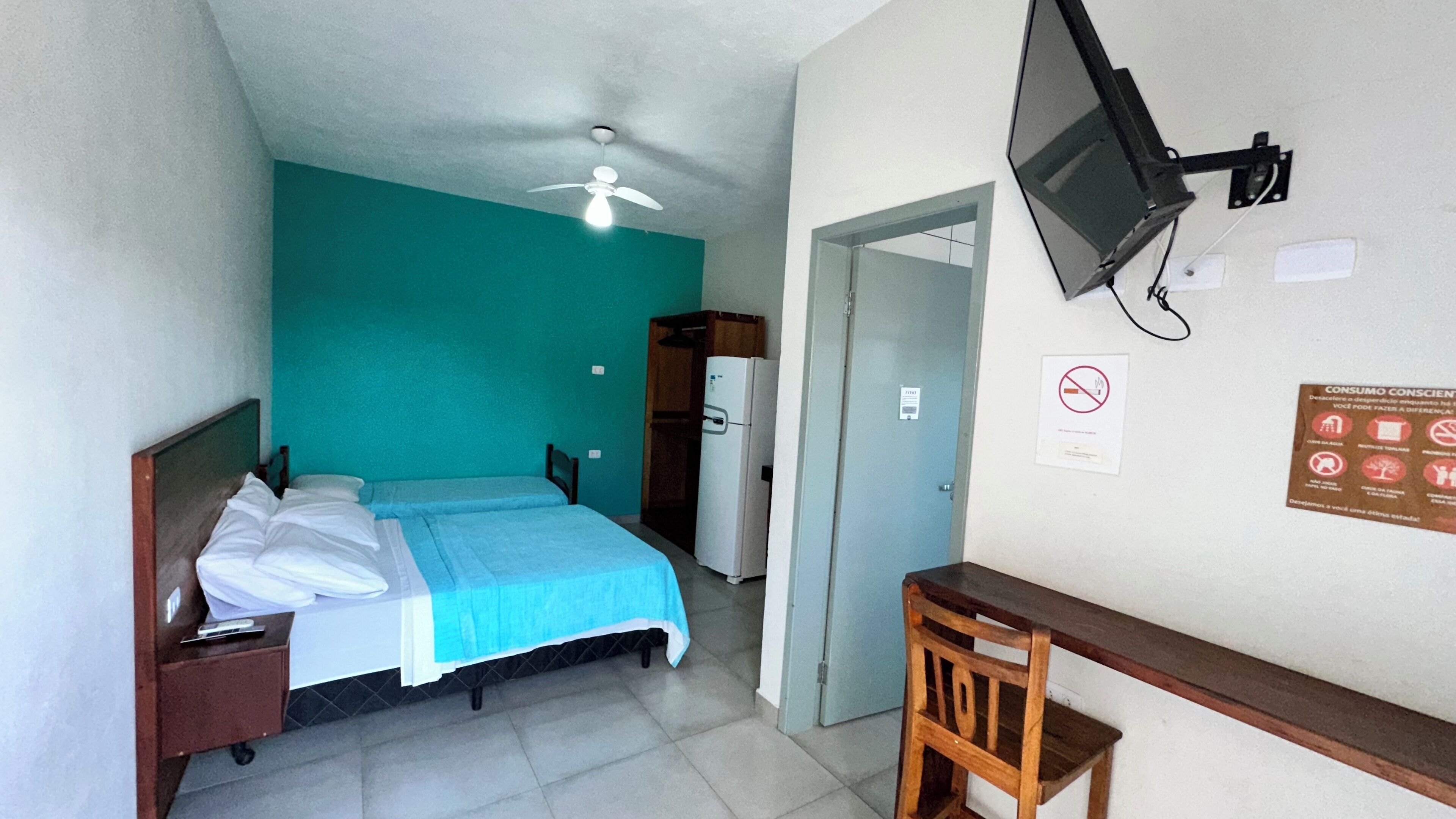 Un dormitorio con cama, escritorio, silla, televisor y puerta.