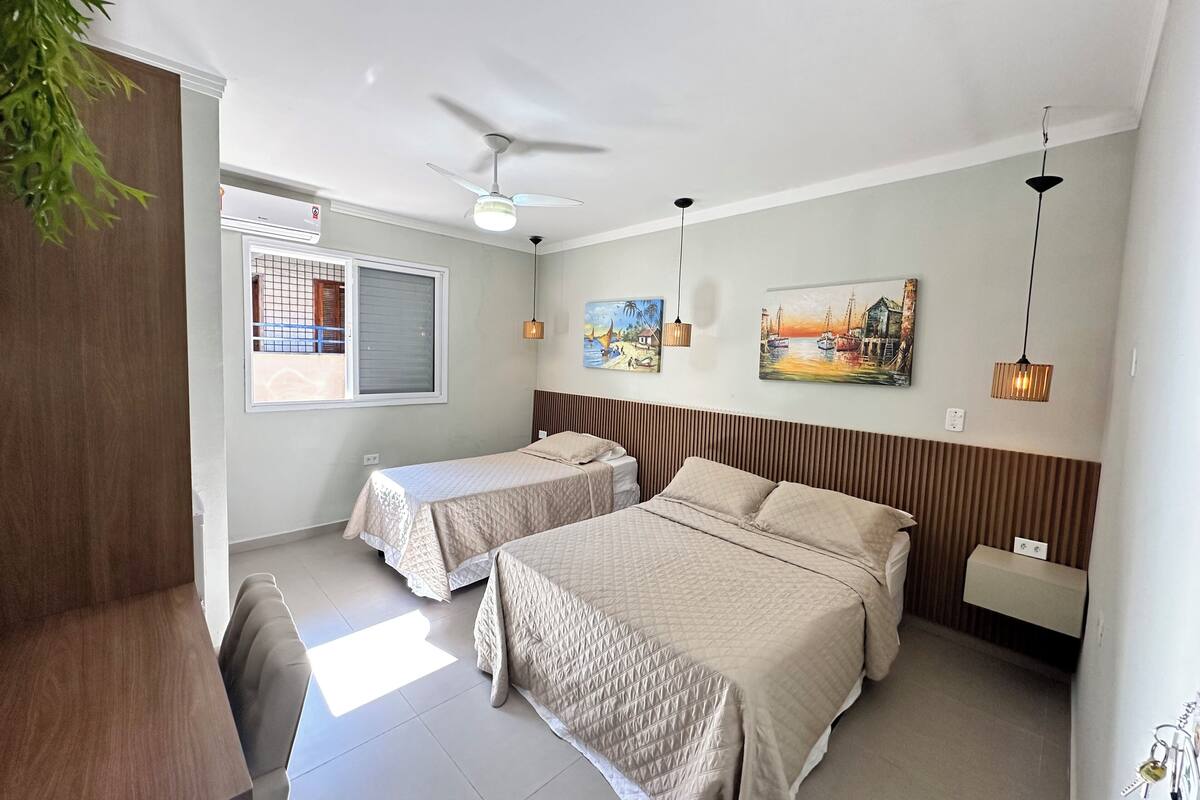 Une chambre d’hôtel avec deux lits, un ventilateur de plafond, une fenêtre avec des stores et des œuvres d’art accrochées aux murs.