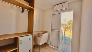 A small room with a wooden shelf, a white chair, a small refrigerator, and a sliding glass door leading to a balcony. - Pousada Praia Grande (Ubatuba)