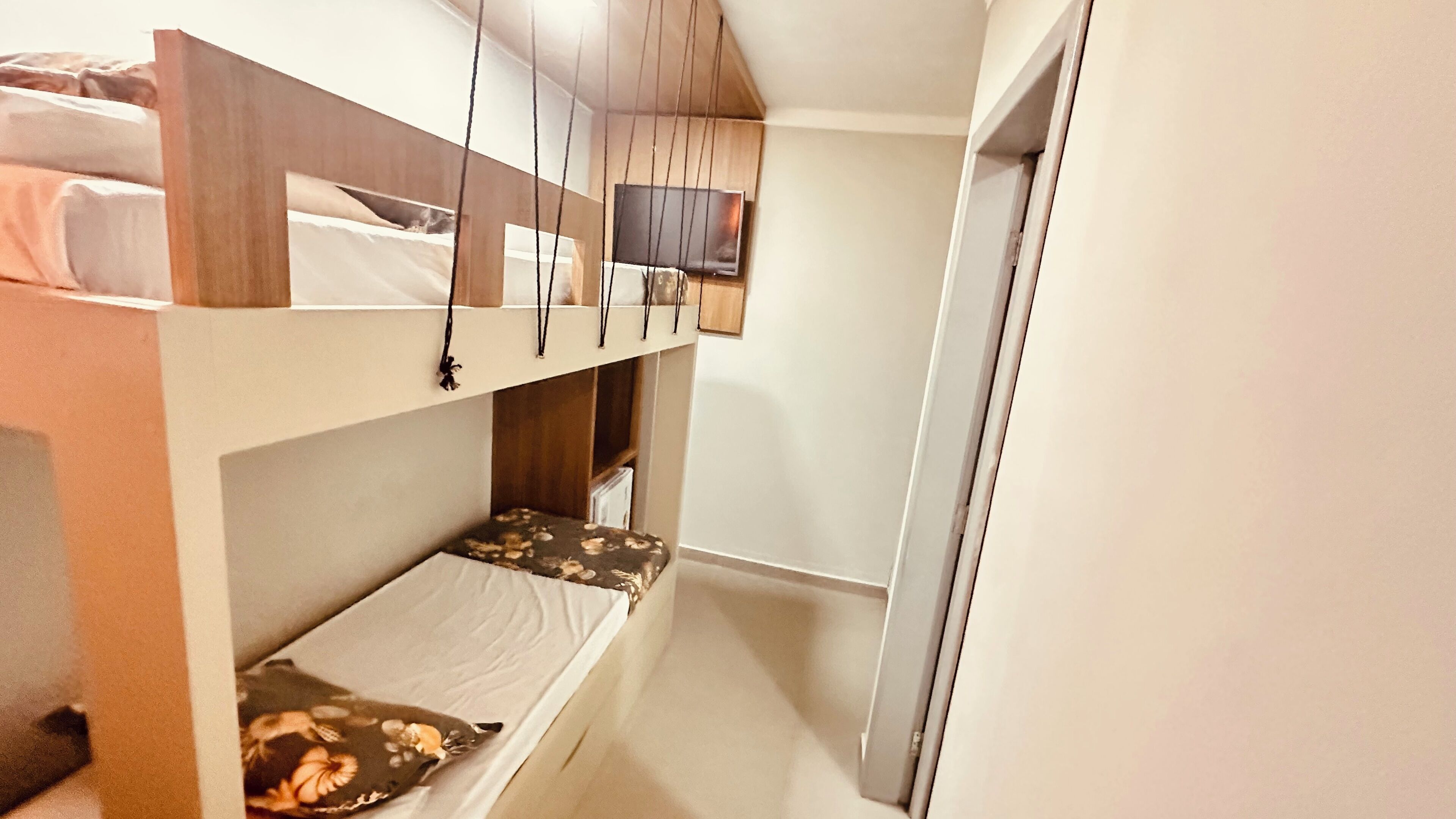 Een kleine kamer met stapelbedden, een houten kastje en een televisie aan de muur.