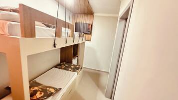 Een kleine kamer met stapelbedden, een houten kastje en een televisie aan de muur.