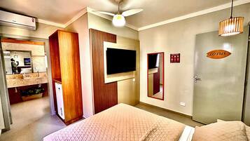 A hotel room with a bed, a television mounted on the wall, a mirror, a wardrobe, and a door with a sign.