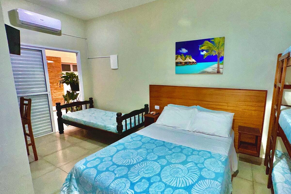 Une chambre avec deux lits, un tableau représentant une scène de plage et une fenêtre donnant sur une plante à l’extérieur.