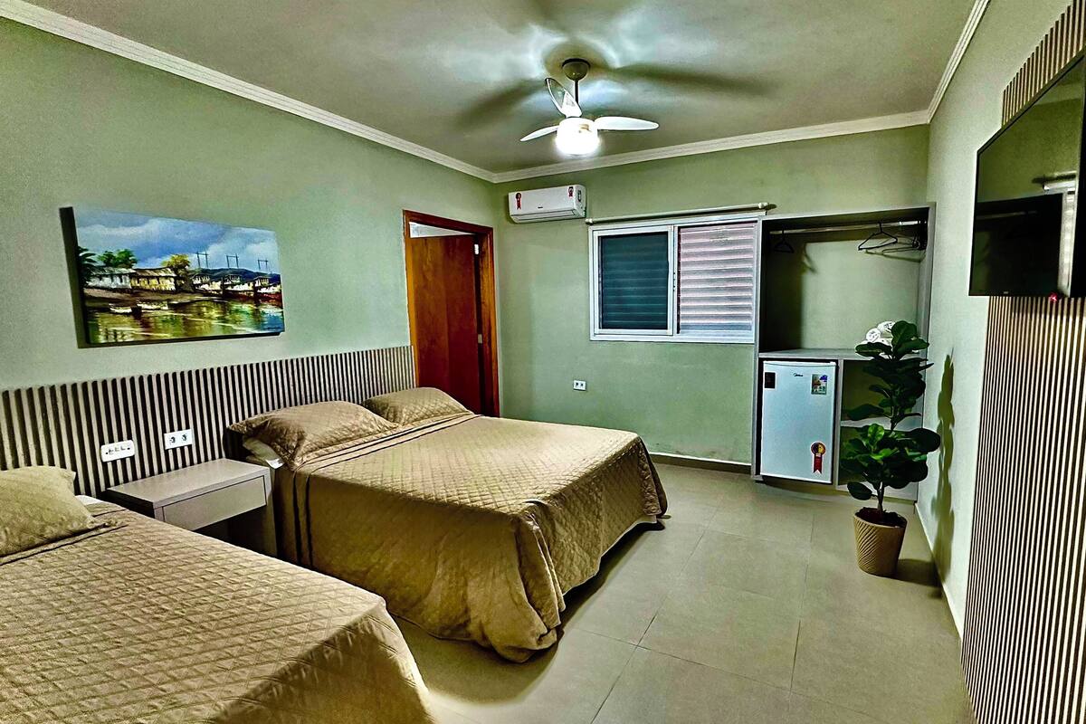 Une chambre d’hôtel avec deux lits, un petit bureau, un ventilateur de plafond, une fenêtre avec des stores, un téléviseur fixé au mur et un petit réfrigérateur.