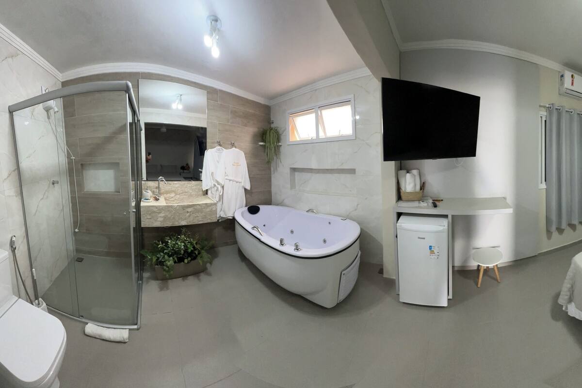 Une salle de bain moderne avec une douche à parois de verre, des toilettes sur pied, une baignoire et un petit réfrigérateur.