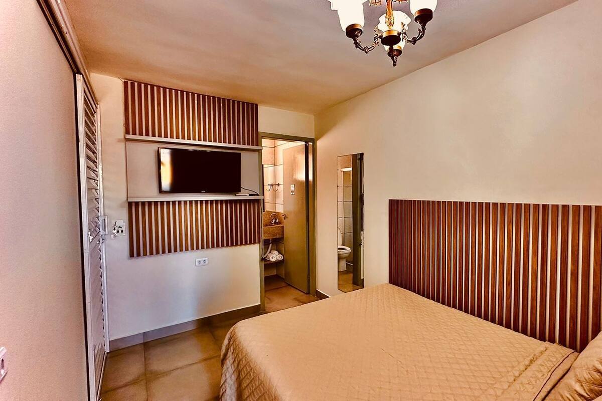 Une chambre à coucher avec un lit, un téléviseur fixé au mur et une tête de lit en bois.