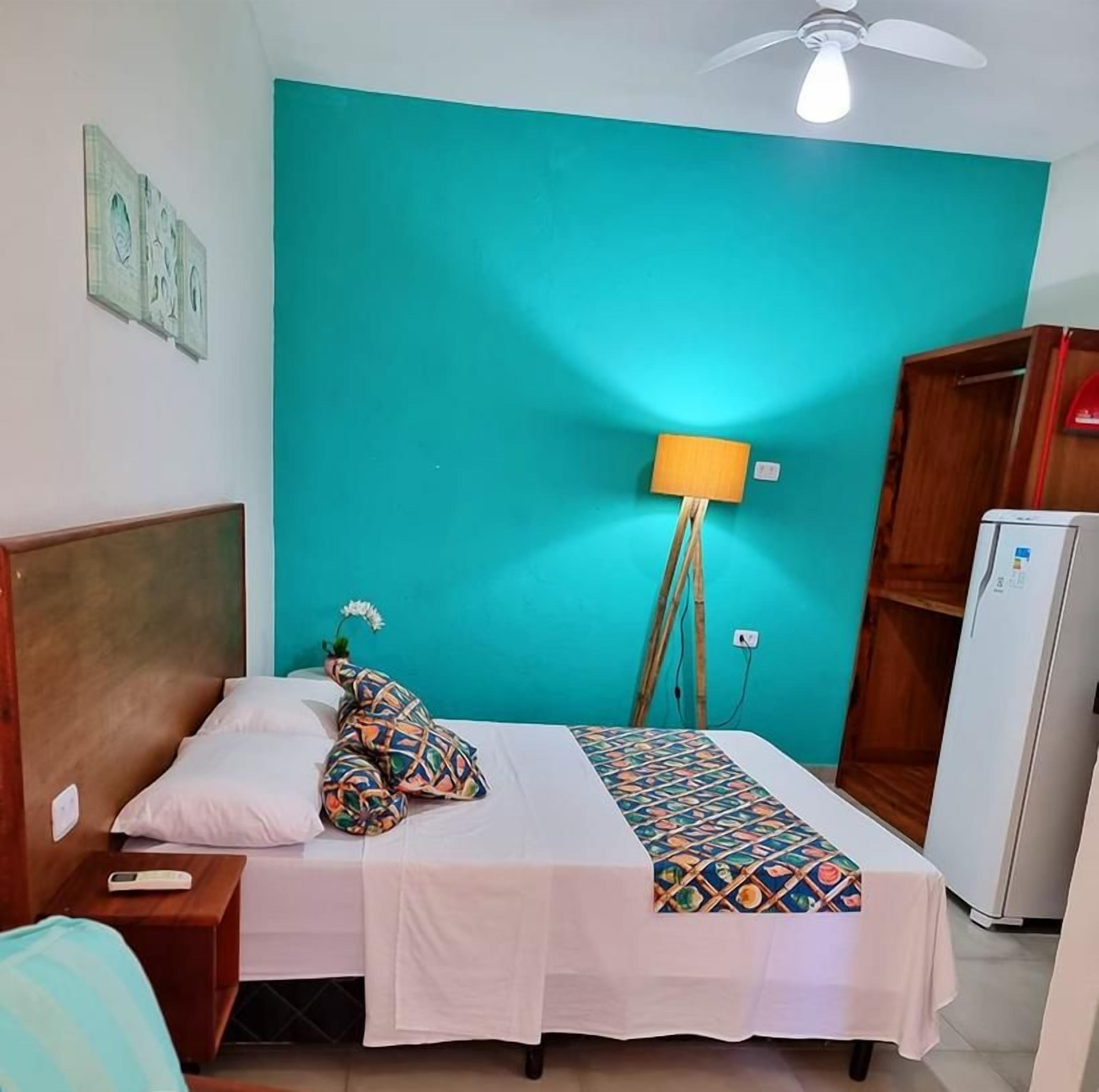 Un dormitorio con cama, mesita de noche, lámpara, armario y refrigerador.