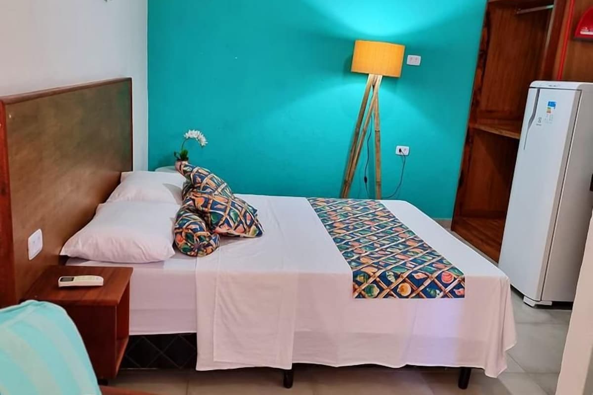 Un dormitorio con cama, mesita de noche, lámpara, armario y refrigerador.