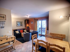 Een knus woongedeelte met een bank, een eettafel en stoelen. Er staat een houten kast en er hangt een lijst met een afbeelding aan de muur.