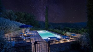 A swimming pool with a stone deck, surrounded by a metal fence, and a night sky with stars above.