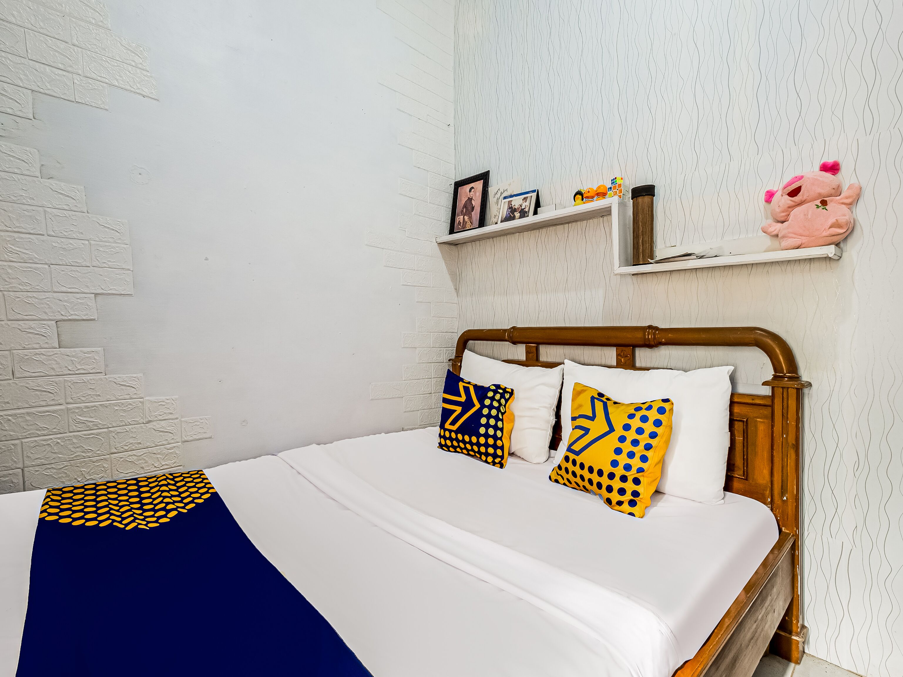 A neatly made bed with a white and blue bedspread, a wooden headboard, and decorative pillows with geometric patterns.