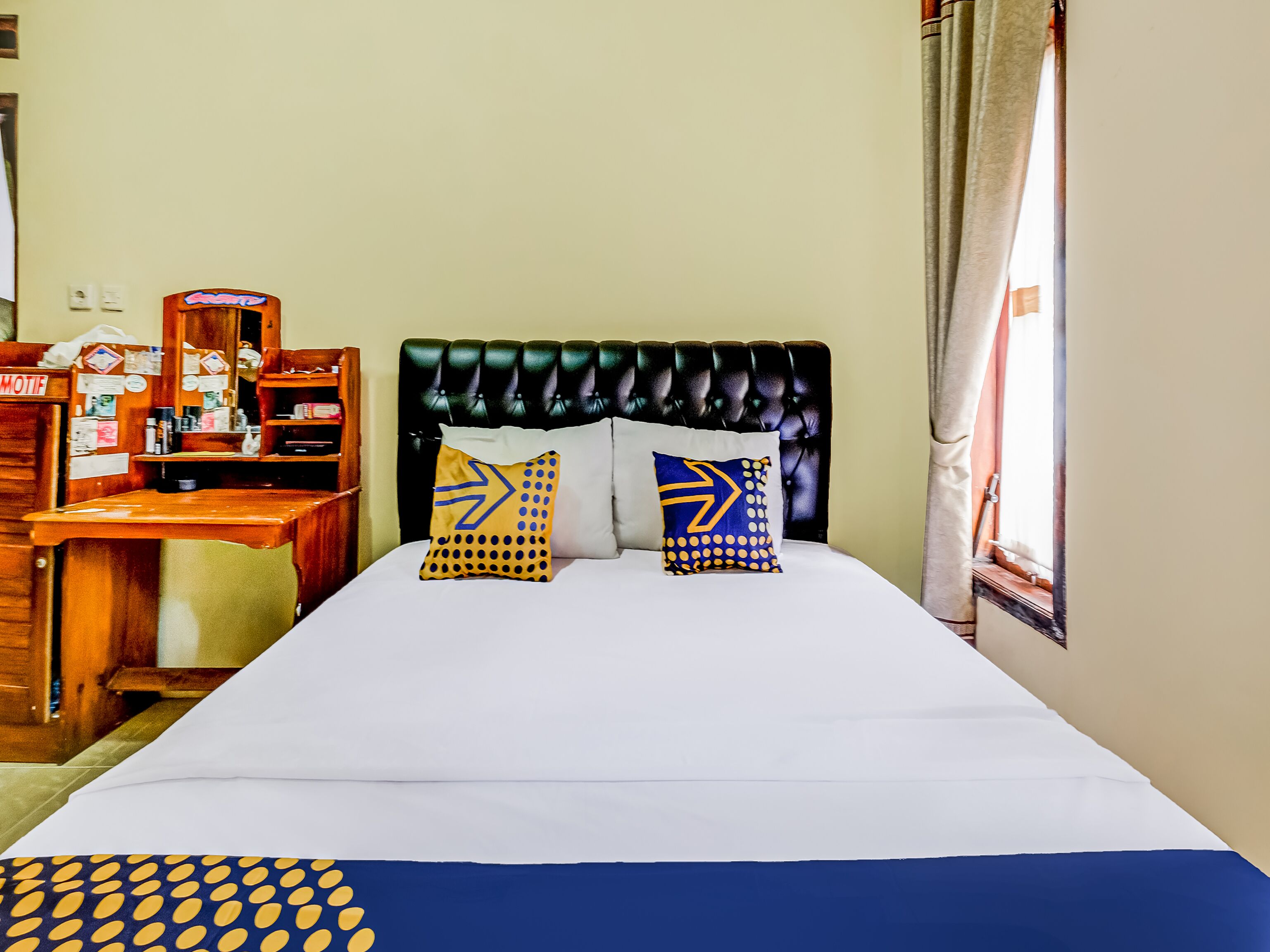 Une chambre d’hôtel avec un lit, deux oreillers ornés de motifs en forme de flèche, un bureau en bois et une fenêtre avec des rideaux.
