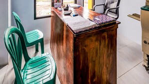 A wooden desk with a calendar, a calculator, and a notebook. There are two green plastic chairs and a black office chair. - Hotel O Desa Wisata Santanamekar (Cisayong)