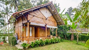 A rustic wooden house with a thatched roof, surrounded by lush greenery and a small pond. - Hotel O Desa Wisata Santanamekar (Cisayong)