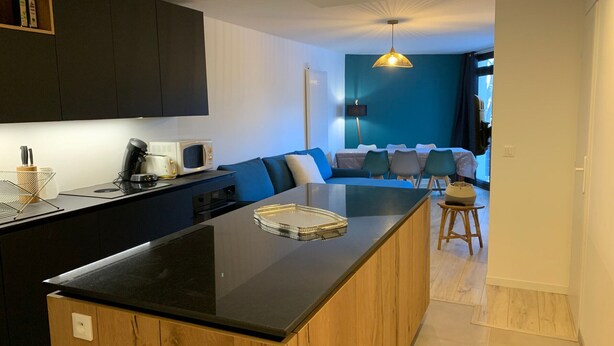A modern kitchen with a central island, dark cabinets, and a dining area with a sofa and chairs. - Beautiful 3-room apt, renovated, central, facing slopes, 6 pers., balcony, parking (Pra-Loup)