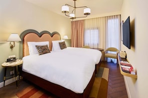 A hotel room with a large bed, bedside lamps, a television, a chair, and a small table with a telephone.