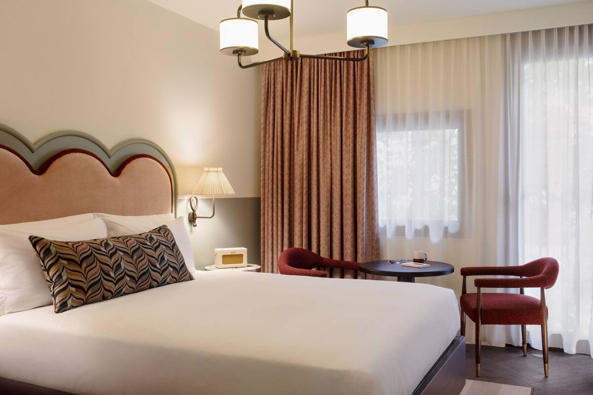 A hotel room with a large bed, a desk with a chair, a lamp, and a window with curtains.