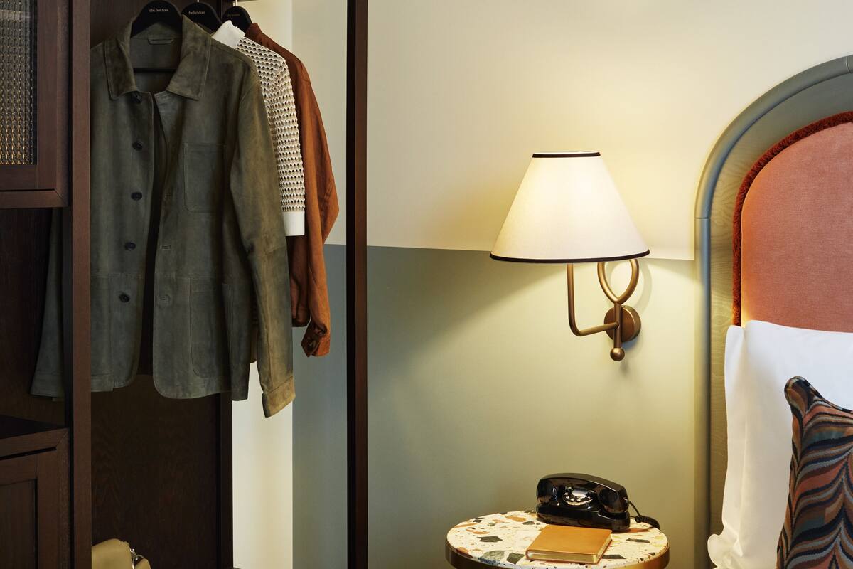 A hotel room with a wardrobe, a bedside table with a lamp, a telephone, and a bed with a pillow.