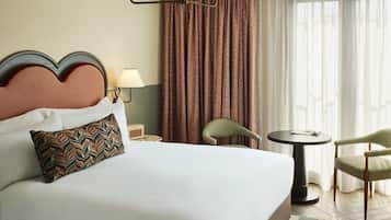 Habitación de hotel con una cama grande, dos sillones, una mesita, una lámpara y vistas al exterior a través de cortinas.