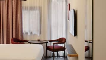 A hotel room with a large bed, a desk, two chairs, a mirror, and a television.