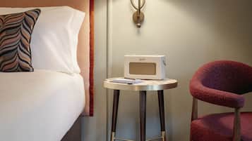 A hotel room with a bed, a table with a radio, a lamp, and a chair.