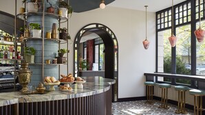 A bar area with a marble counter, shelves with plants, and hanging pendant lights. - The Hoxton, Berlin (Berlin)