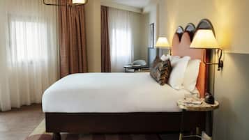 Habitación de hotel con una cama grande, una mesita de noche con lámpara, una silla y un escritorio con teléfono.
