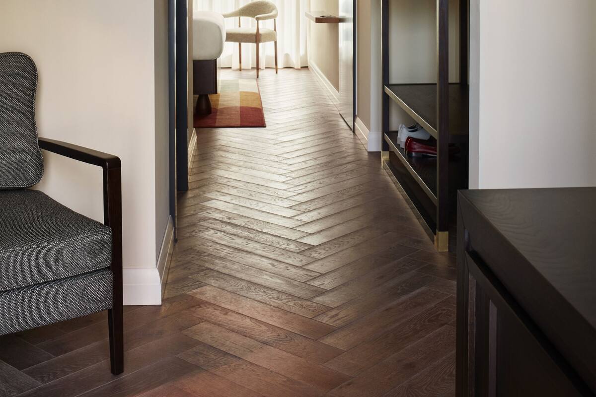 A hallway with a wooden floor, a chair, a coat rack, and a bed.