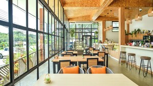 Um café espaçoso com grandes janelas, teto de madeira e diversos tipos de assentos, incluindo mesas e banquetas.