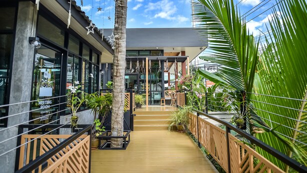 Um edifício moderno com deck de madeira, janelas de vidro e plantas tropicais.