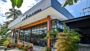 Café e bistrô com design moderno, grandes janelas e área externa com mesas rodeada por plantas tropicais.