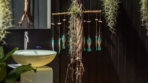 Um banheiro com pia branca, espelho e plantas penduradas.