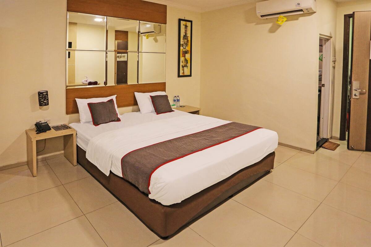 Une chambre d’hôtel avec un grand lit, une table de chevet avec un téléphone, une commode, un miroir et un appareil de climatisation.